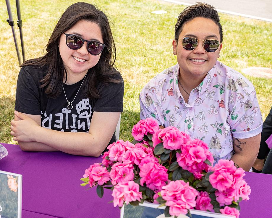 Two 博彩平台网址大全 employees celebrate AANHPI Heritage Month at a table with pink flowers